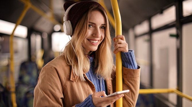 Glimlachende vrouw in bus luistert naar true crime-podcast waarin iemand wordt onthoofd met bijl