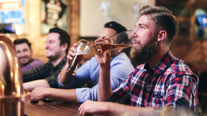 Vriendengroep die ‘flink de bloemetjes buiten gaat zetten’ kijkt met biertje in de hand vanaf barkruk zwijgend naar vrouwen